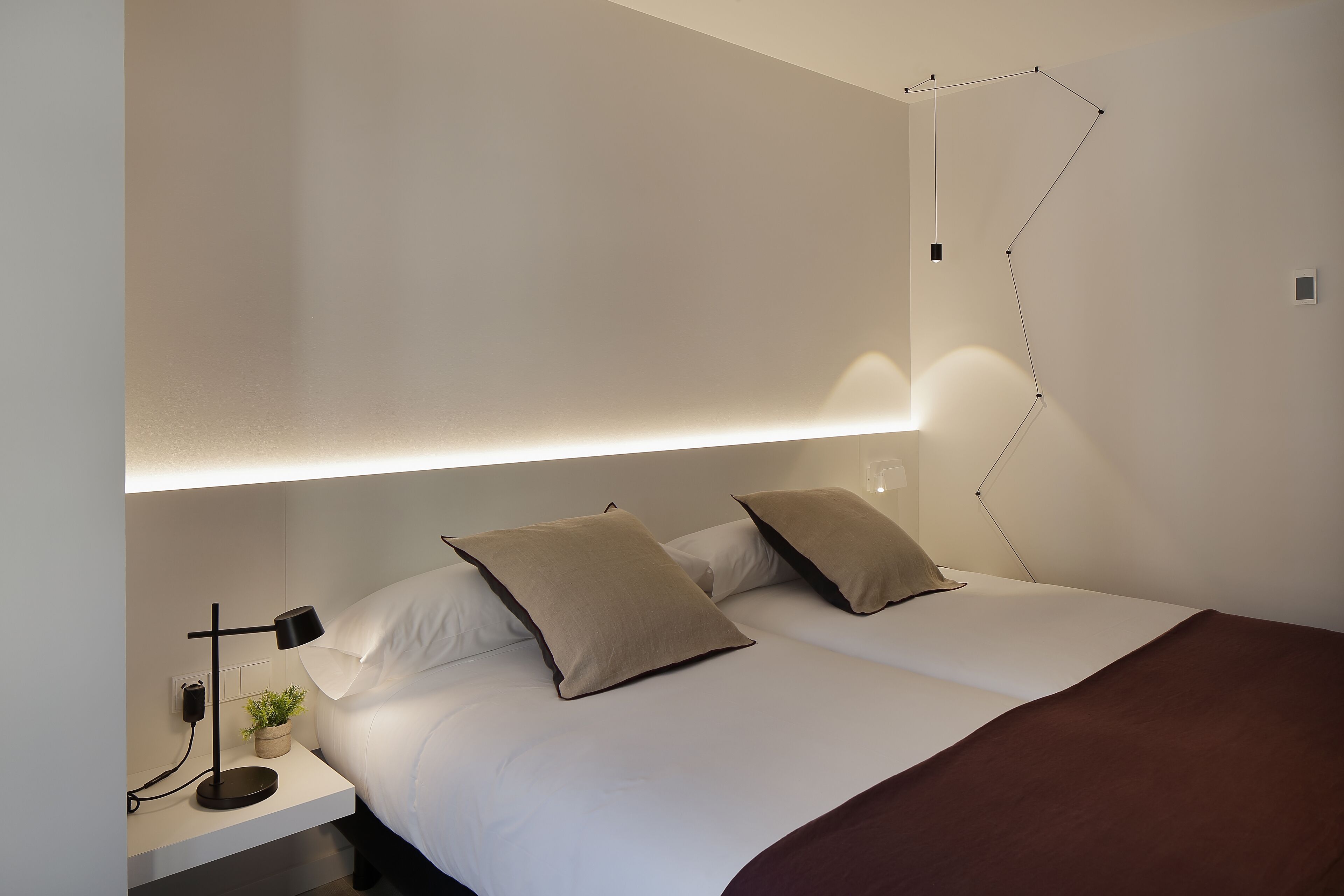 Un dormitorio moderno con cama, mesita de noche, lámpara e iluminación empotrada en la pared.