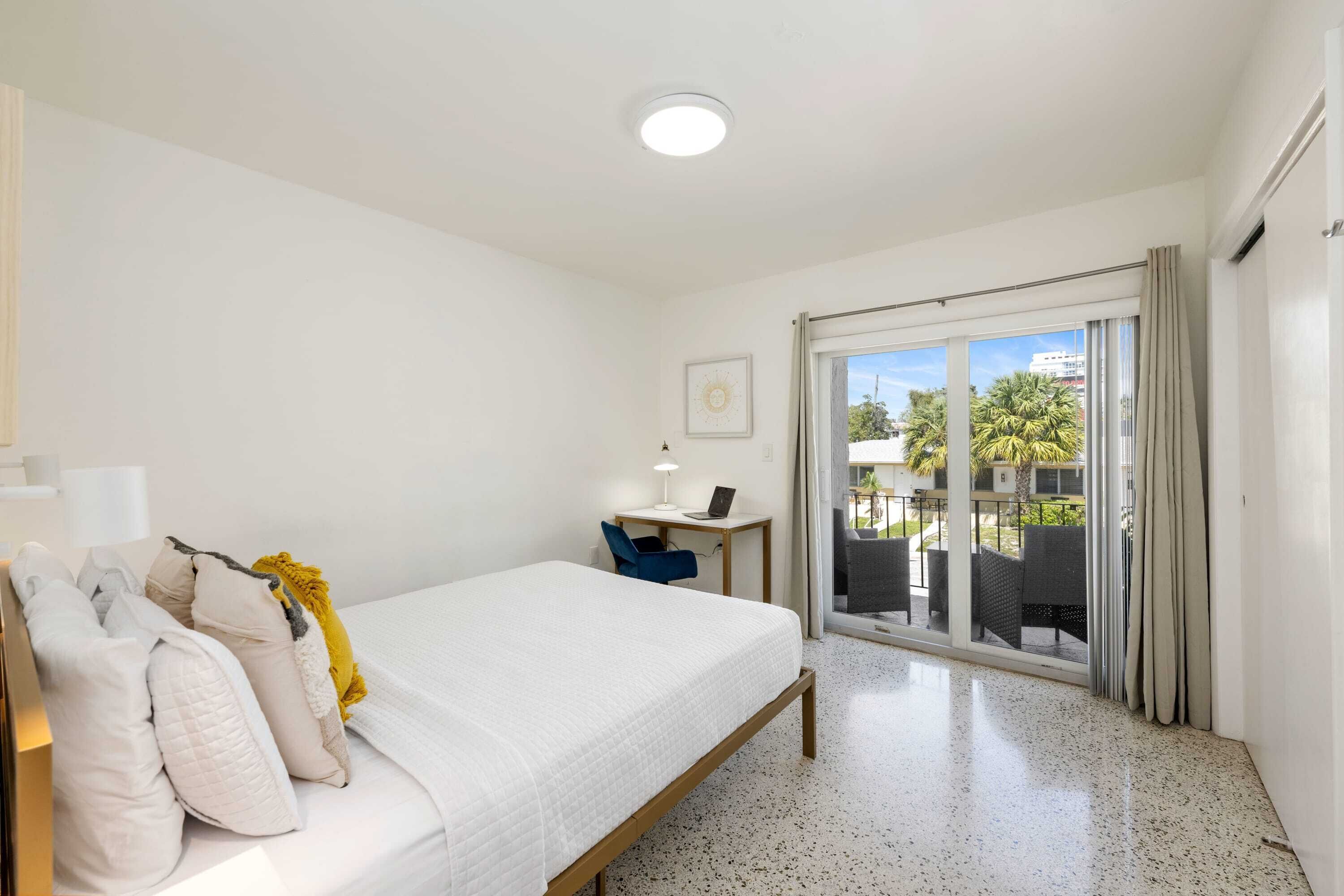 Une chambre d’hôtel avec un lit, un bureau avec un ordinateur portable, une chaise et une vue sur l’extérieur grâce à une porte-fenêtre coulissante.