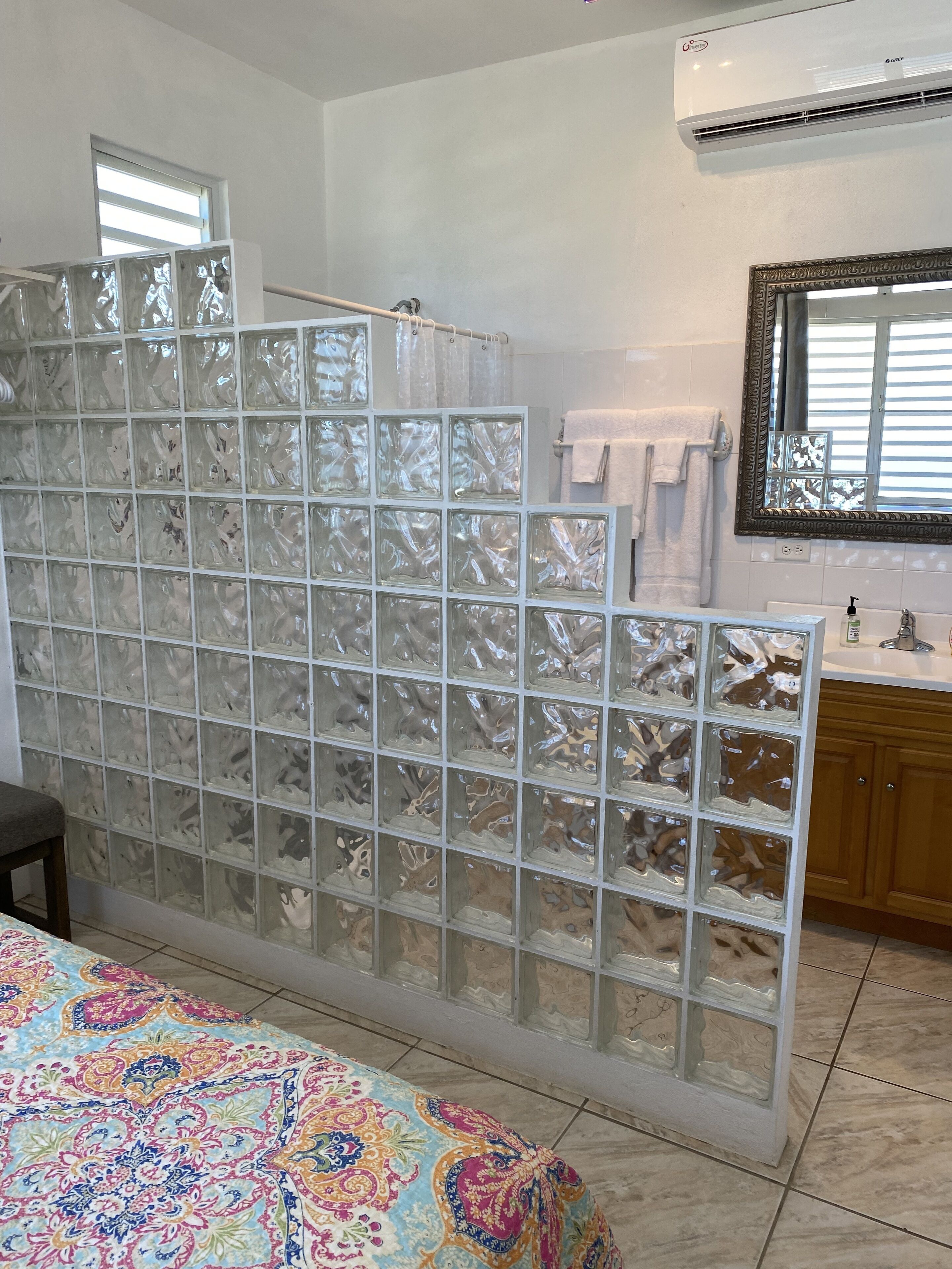 A bathroom with a glass partition, a shower area, a sink with toiletries, and a mirror.