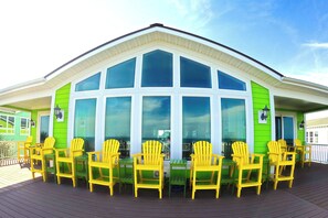 A building with large windows and a covered patio area with yellow chairs and tables. -  OCEAN FRONT HOME w/Heated private Pool, Elevator, 12 Bed/12 Bath, Pet Friendly (Holden Beach)