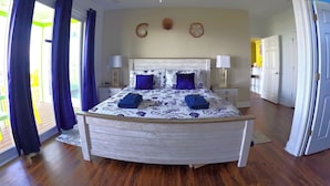 A bedroom with a bed, ceiling fan, and a view of the outdoors.