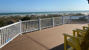 A wooden deck with white railings overlooking a beach.
