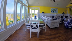 A spacious room with large windows, a dining area, and a seating area with a view of the ocean.