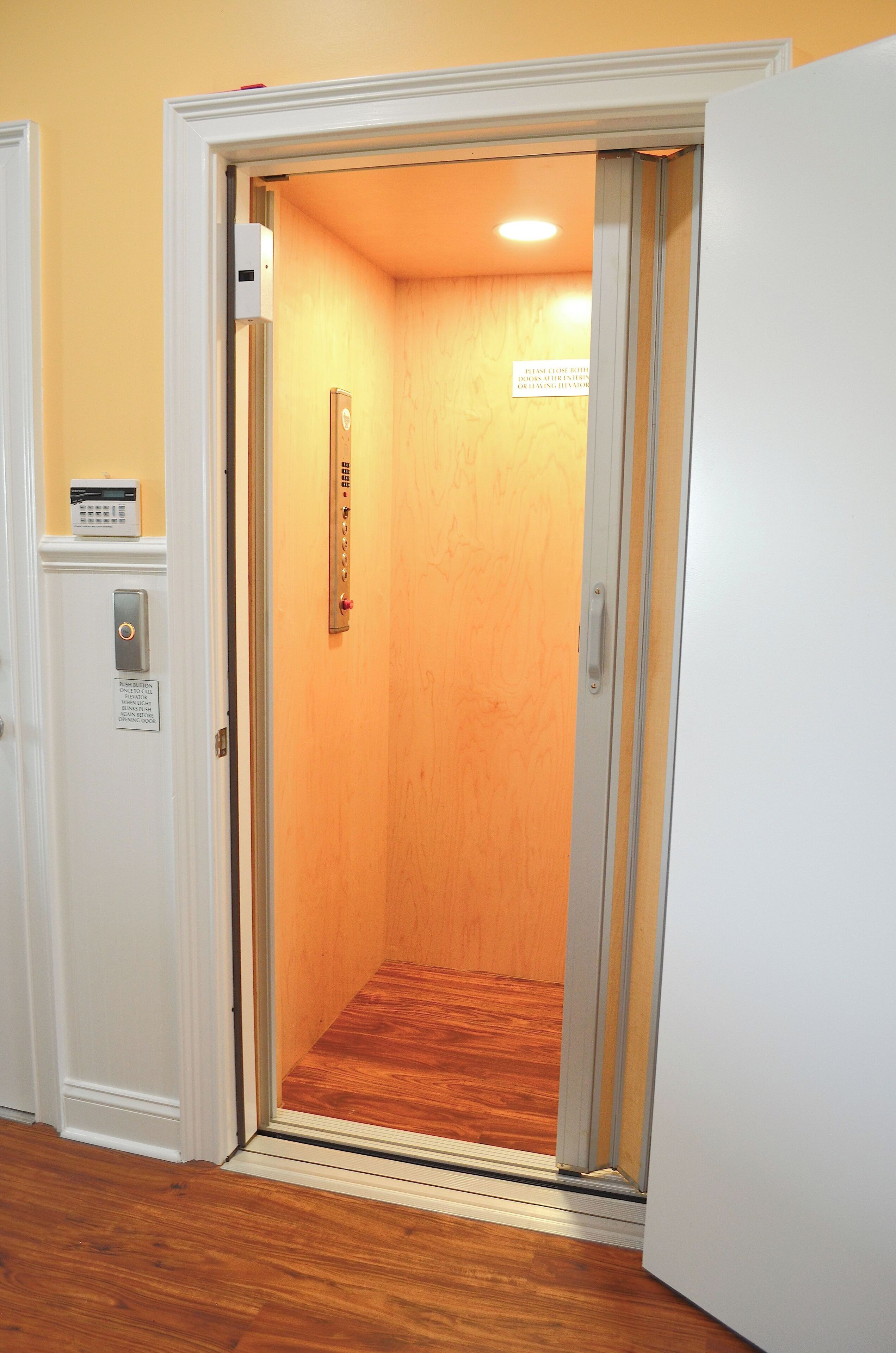 An elevator with a wooden interior, a control panel, and a sign on the wall.