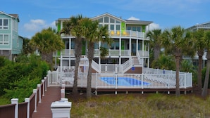 A multi-story beachfront property with a pool, white railings, and palm trees.