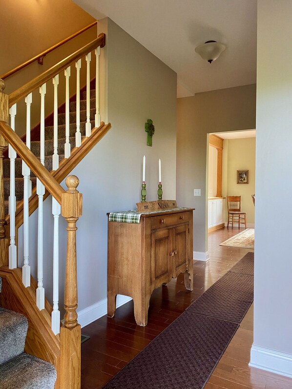 A wooden staircase with white balusters, a wooden cabinet with a green top, and a dark brown rug on a wooden floor. - <1 Mile to Flintfields - 5BR Modern Farmhouse, Pet-Friendly (Williamsburg)