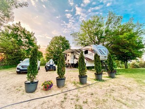 Guests can park their RV and compact vehicle on the dirt path surrounded by lush greenery and potted plants.