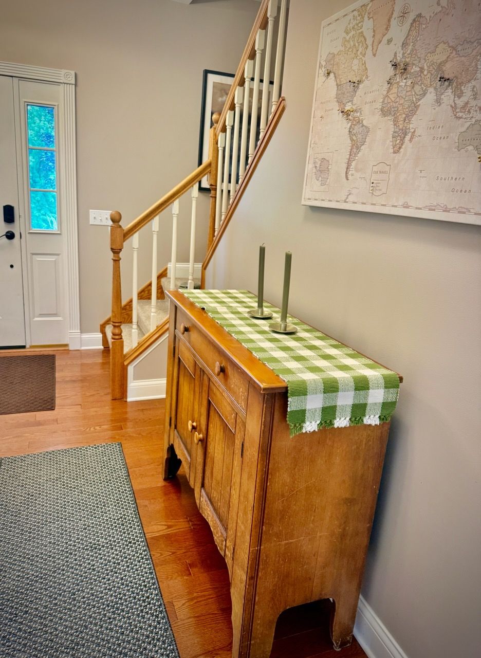 Un mueble de madera con un mantel a cuadros verde y blanco, una escalera con barandillas de madera y un mapa mundial en la pared.