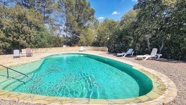 Piscina retangular com borda de pedra, rodeada por espreguiçadeiras brancas e um deck de pedra.