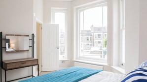 A bedroom with a bed, a dresser, a mirror, and a window with a view of buildings. - Beautiful 2 bed terrace flat close to Greenwich -  Pass the Keys (London)