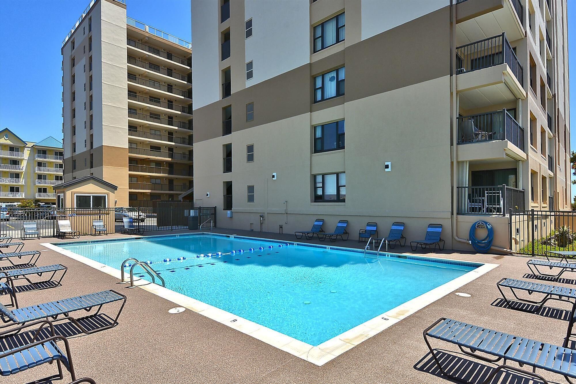 Une piscine avec des chaises longues et un bâtiment doté de nombreux balcons.