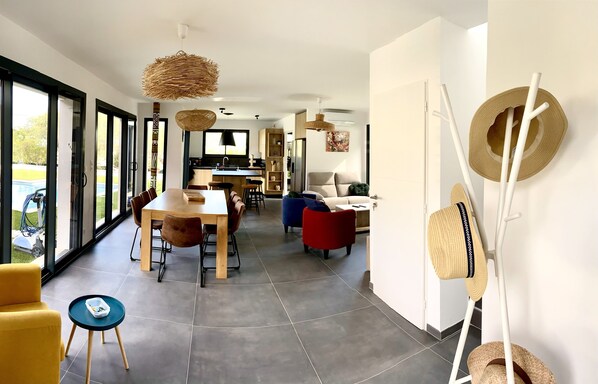 Un salon moderne avec un coin repas, de grandes fenêtres et une vue sur l’extérieur.