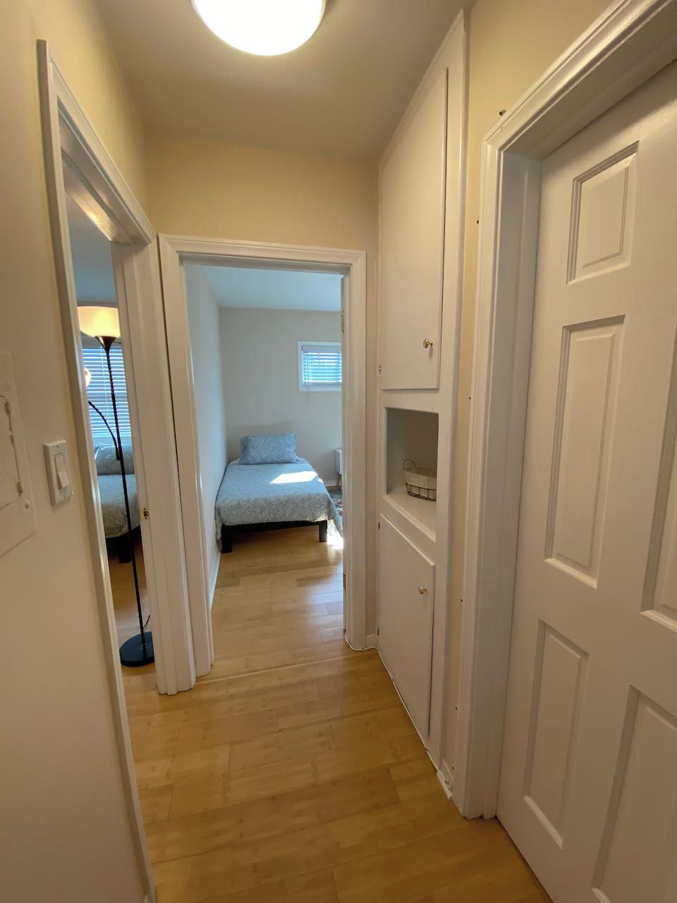 Un corridoio stretto con pavimento in legno che conduce a una camera da letto con un letto e una finestra.