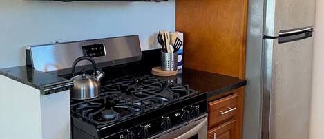 A kitchen with wooden cabinets, a stainless steel microwave, a gas stove, and a stainless steel refrigerator.