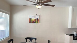 A dining area with a round table, four chairs, a ceiling fan, a poster on the wall, and a trash bin. - Westside turnkey 2 bd apt #6 (Culver City)