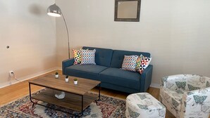 A living room with a blue sofa, a wooden coffee table, patterned ottomans, a floor lamp, and a decorative mirror. - Westside turnkey 2 bd apt #6 (Culver City)