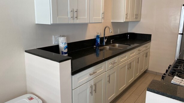 A modern kitchen with white cabinets, a black countertop, stainless steel sink, and a gas stove. - Westside turnkey 2 bd apt #6 (Culver City)