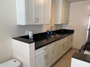 Une cuisine moderne avec des meubles blancs, un plan de travail noir, un évier en acier inoxydable et une cuisinière à gaz.