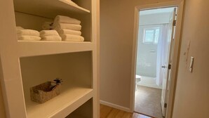 Un pasillo con un mueble blanco donde hay toallas dobladas y una cesta.