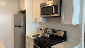 Una cocina con armarios blancos, un refrigerador de acero inoxidable, un microondas y una estufa a gas.