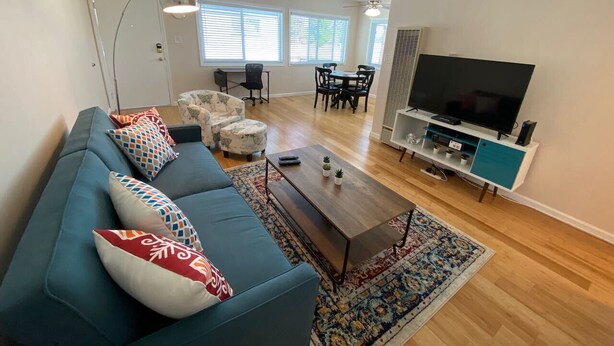 A modern living room with a blue sofa, patterned cushions, a coffee table, and a TV on a stand.