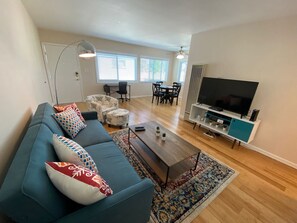 Un salon moderne avec un canapé bleu, des coussins à motifs, une table basse et un téléviseur posé sur un meuble.
