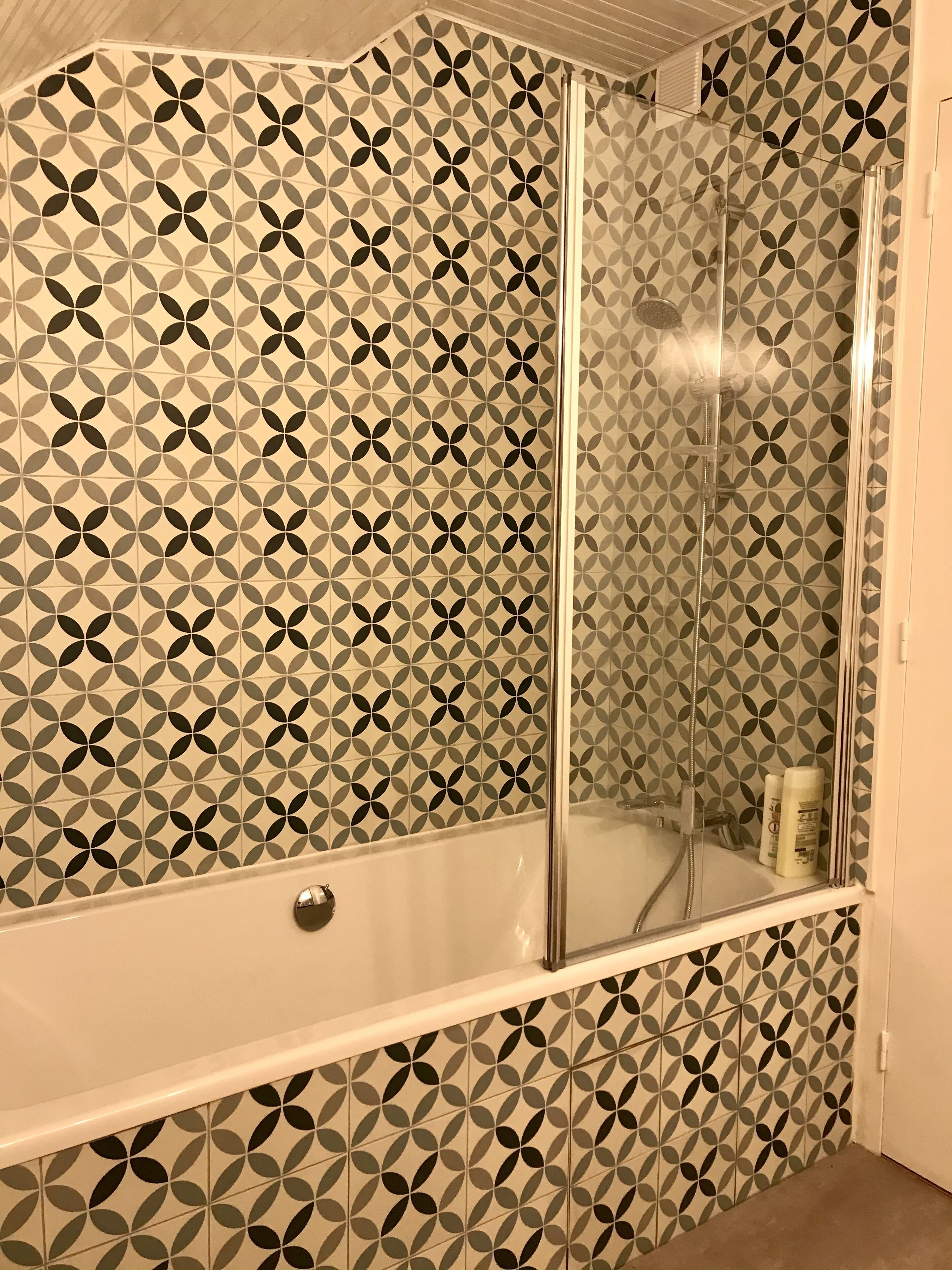 Ein Badezimmer mit geometrischem Fliesenmuster, einer Duschkabine aus Glas und einer Badewanne.