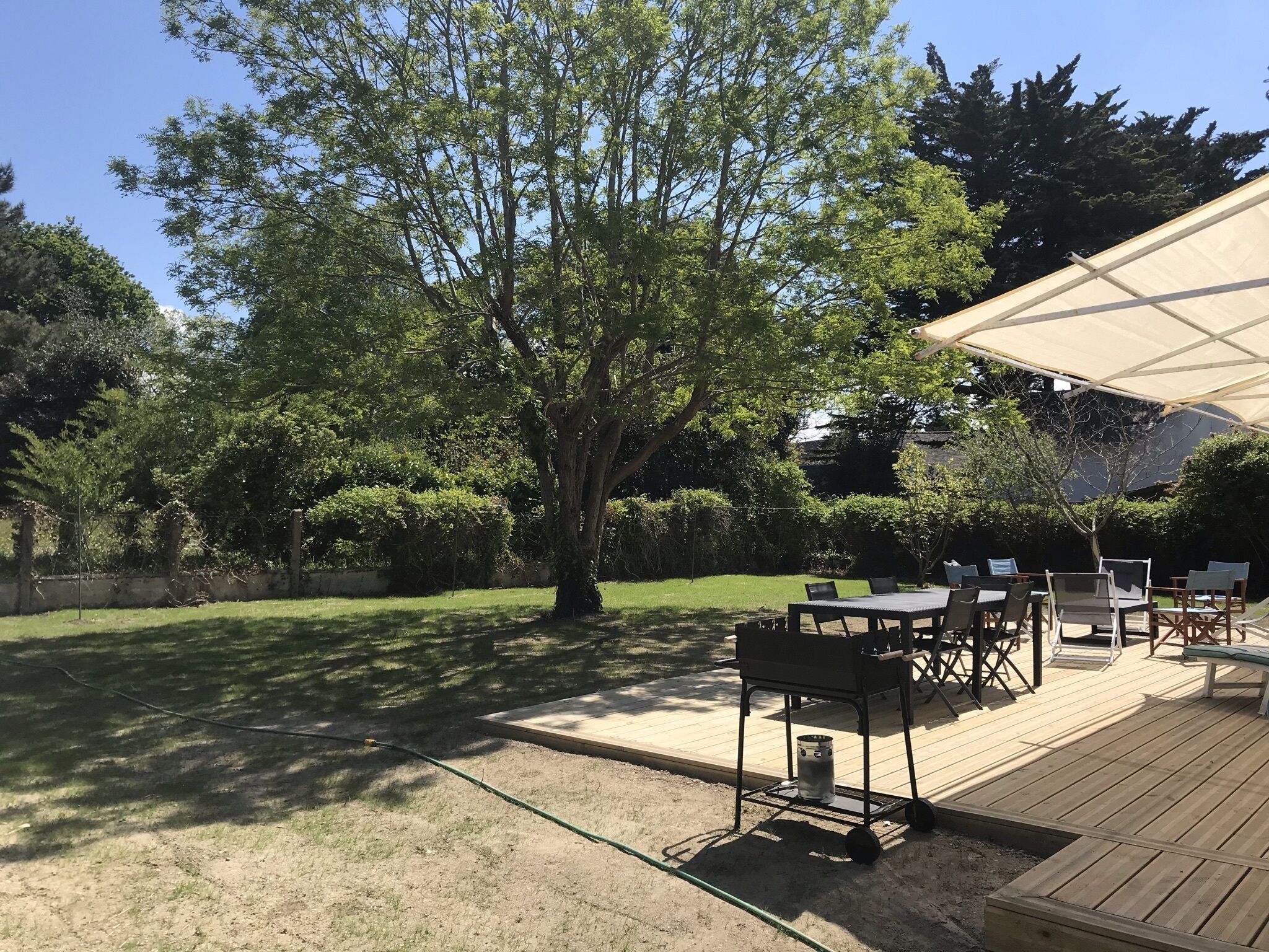 An outdoor patio area with a wooden deck, a table with chairs, and a large umbrella providing shade.