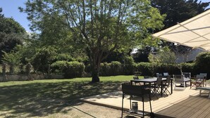 Ein Außenbereich mit einer Holzterrasse, einem Tisch mit Stühlen und einem großen Sonnenschirm, der Schatten spendet.