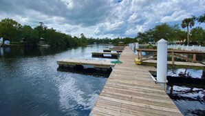 A wooden dock extending into calm water, surrounded by trees and a cloudy sky.