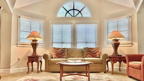 A living room with a sofa, two lamps, a coffee table, and a window with blinds.