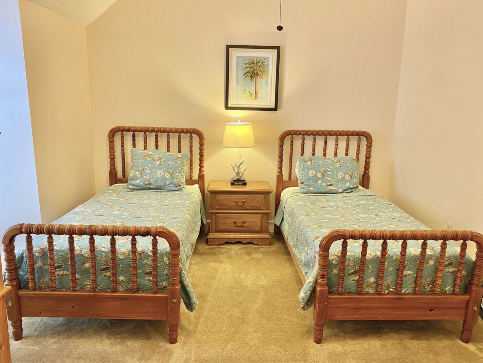 A bedroom with two wooden beds, a nightstand with a lamp, and a framed picture on the wall.