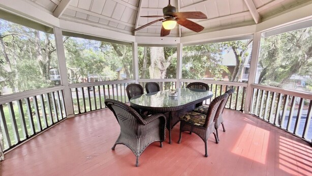A covered outdoor dining area with a round table and chairs, a ceiling fan, and a view of trees and a house. - Steinhatchee Landing - Victorian Cottage 9 Upstairs (Steinhatchee)