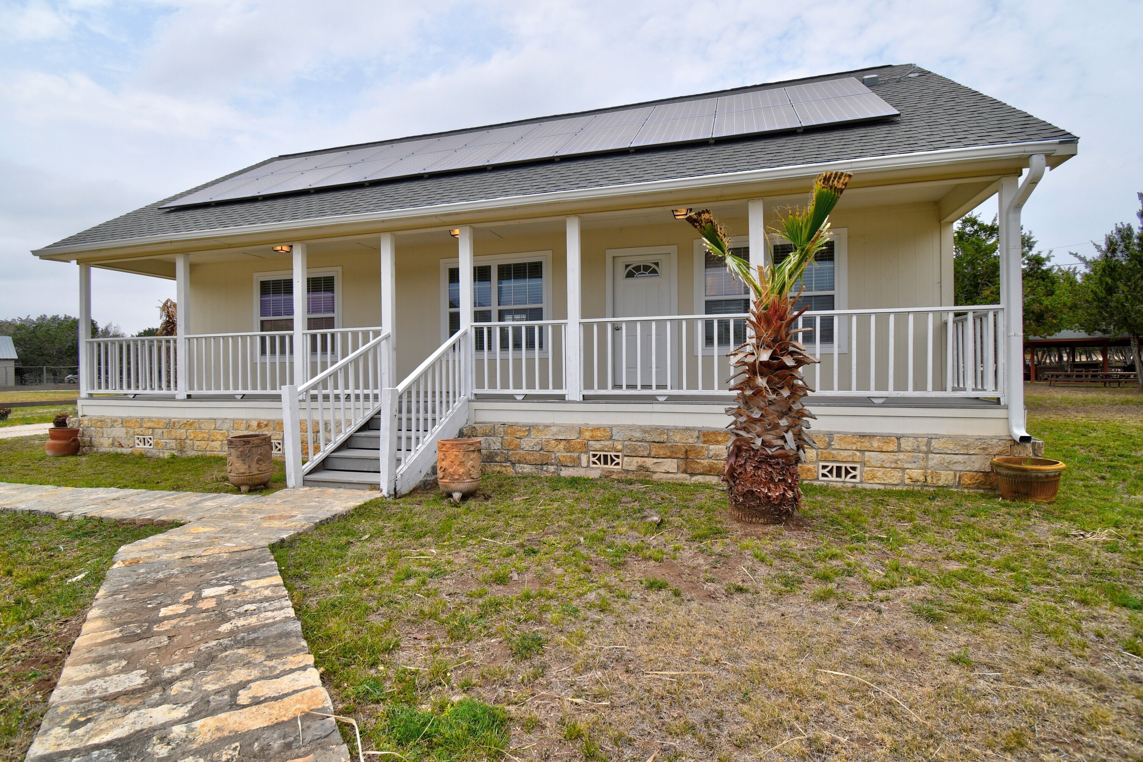 A single-story house with a covered porch, a stone foundation, and a small palm tree.