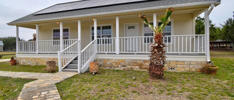 A single-story house with a covered porch, a stone foundation, and a small palm tree.