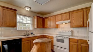 A kitchen with wooden cabinets, a dishwasher, an oven, and a window with blinds. - Cottage House, 3BR/2BA, Sleeps 8, Porch, Grill, Firepit (Kerr County)