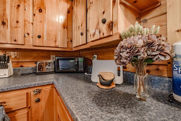 Una cocina con armarios de madera, microondas, tostadora y un jarrón con flores secas.