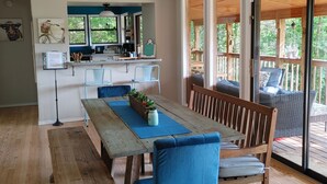 Ein Essbereich mit einem Holztisch, blau gepolsterten Stühlen, einem Deckenventilator und Blick auf eine Terrassenfläche.