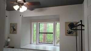 Ein Schlafzimmer mit Bett, Fensterbank, Deckenventilator und Bildern an den Wänden.