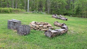 A grassy area with a stack of stones and logs, surrounded by trees. - Luxury 5th Wheel Glamping In Style In Historic Mentone,  Alabama (Mentone)