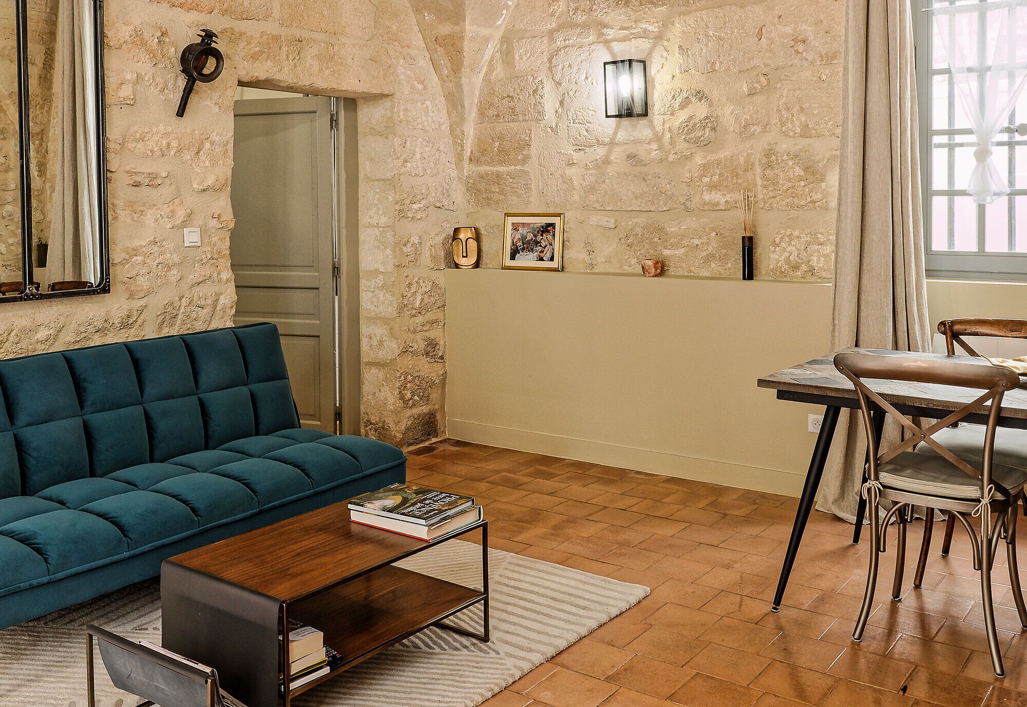 A living room with a teal sofa, a wooden coffee table, and a dining area with a metal chair and table.