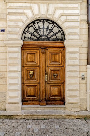 A large wooden double door with a decorative metal arch above it, set in a stone building facade.