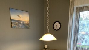 Uma área de refeições com mesa de madeira e cadeiras acolchoadas, luminária pendente, relógio e janela com vista.