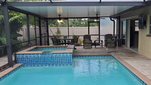 A covered outdoor swimming pool with a patio area, including a table and chairs, and a view of the backyard. - Naples Beach house with heated Pool & Spa (Naples)