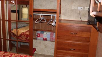 A compact bedroom with a bed, a dresser, and a hanging clothes rack.