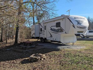 A white RV with 'Avalanche' branding parked in a wooded area with a picnic table and fire pit nearby. - Luxury 5th Wheel Glamping In Style In Historic Mentone,  Alabama (Mentone)