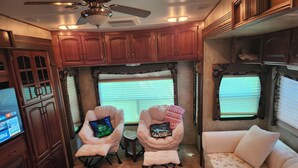 Interior d'una caravana acollidora amb armaris de fusta, dues butaques amb coixins, una taula petita i un sofà amb un llençol floral.