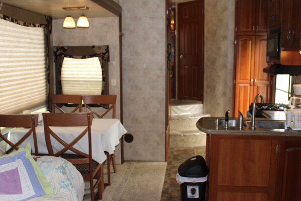 A cozy kitchen with wooden cabinets, a sink, and a dining area with chairs and a table. - Luxury 5th Wheel Glamping In Style In Historic Mentone,  Alabama (Mentone)