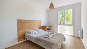 A minimalist bedroom with a wooden headboard, a desk, and a large window.