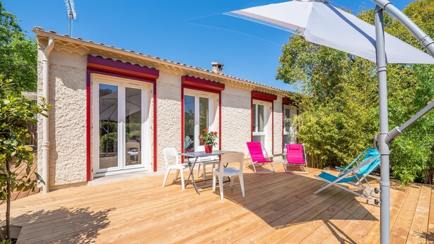 A wooden deck with a table and chairs, a covered area with a white umbrella, and a pool chair.